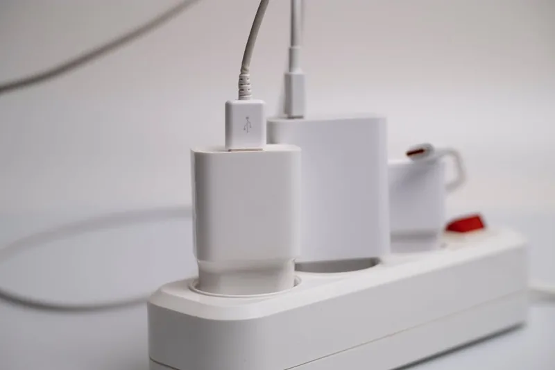 Eine Hand steckt ein Netzkabel in eine 3-fach Steckdosenleiste an einem Schreibtisch.