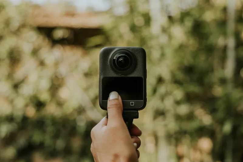Eine Person hält eine 360 Grad Kamera während einer Wanderung, bereit, die gesamte Umgebung aufzunehmen.
