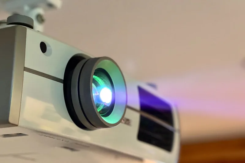 Eine Hand hält eine Fernbedienung und steuert die Einstellungen eines 4K Beamers in einem Heimkino.