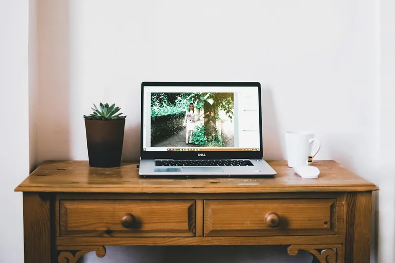 Aufgeräumter Schreibtisch im Home-Office mit Laptop und Pflanzen, schafft ruhige Arbeitsatmosphäre.