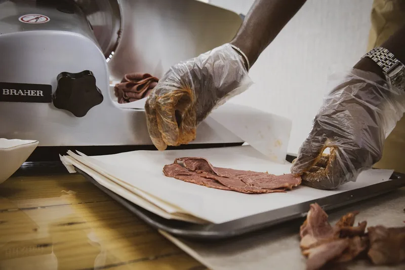 Eine Hand bedient einen Allesschneider, um frisches Brot in gleichmäßige Scheiben zu schneiden.