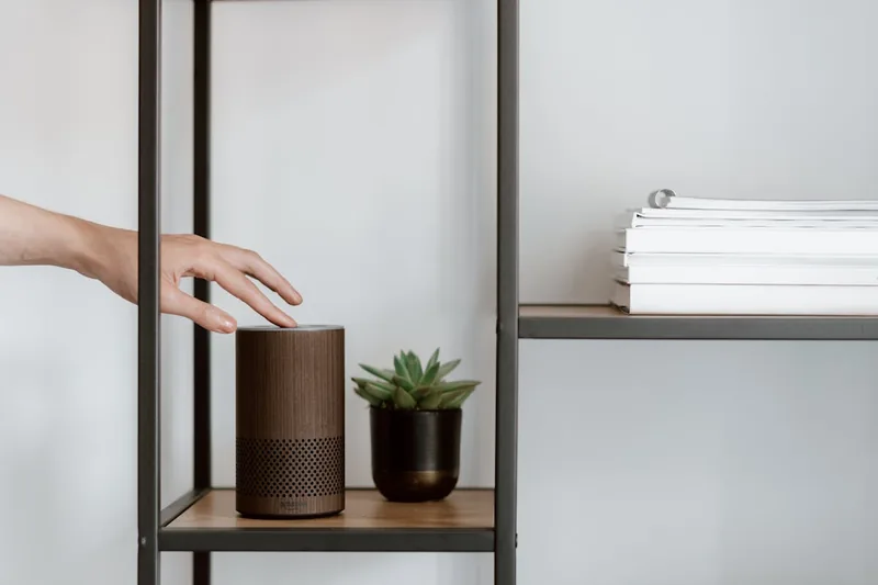 Eine Person interagiert mit einem smarten Lautsprecher per Sprachbefehl im Wohnzimmer.