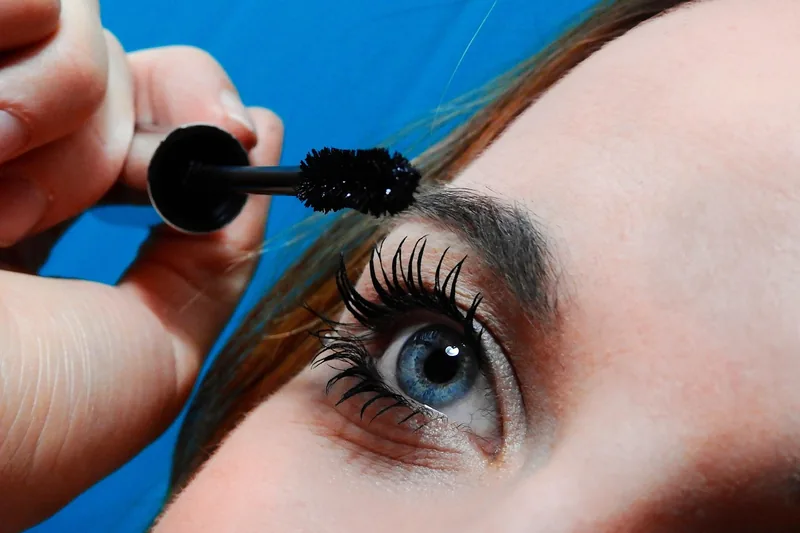 Eine Frau trägt Wimperntusche auf ihre Wimpern auf, fokussiert auf die Anwendung des Kosmetikprodukts.