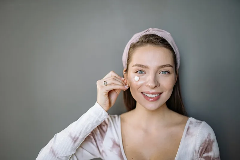 Eine Person trägt vorsichtig Augencreme mit dem Finger auf die Haut unter dem Auge auf.