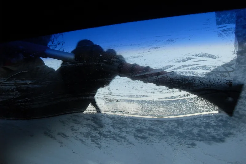 Person benutzt Auto Eiskratzer zur Scheibenreinigung im Winter