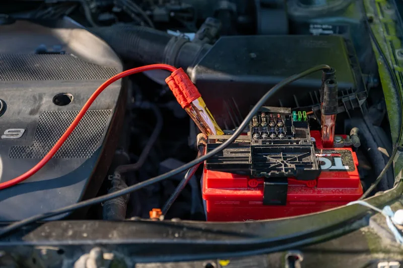 Eine Hand setzt eine 100Ah Autobatterie vorsichtig in den Motorraum eines Fahrzeugs ein.