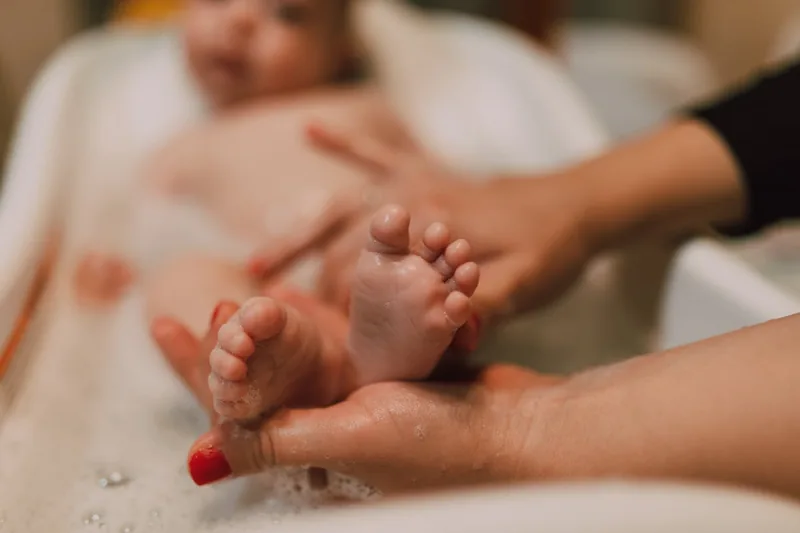 Eine Hand stützt ein Baby im Badewannensitz, das Baden ist sicher und komfortabel.