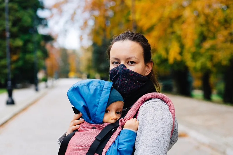 Ein Elternteil trägt ein Baby in ergonomischer M-Position in einer Trage, Nahaufnahme Rücken.