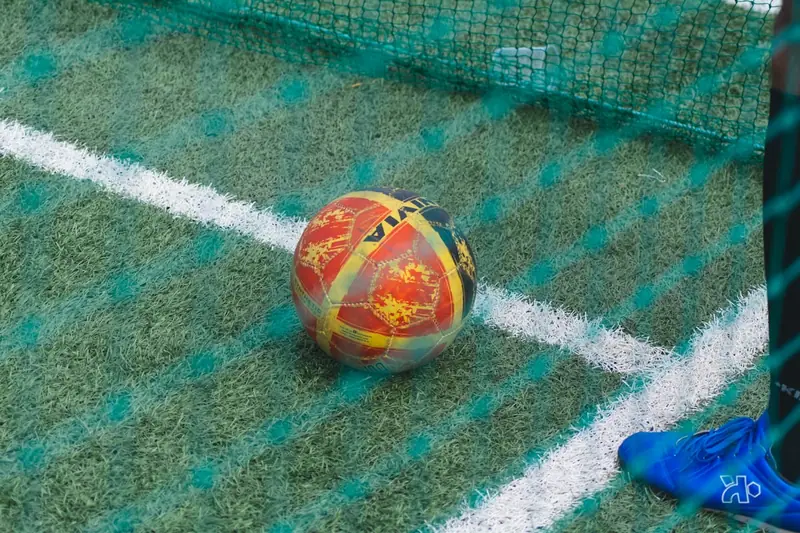Eine Hand pumpt einen Fußball mit einer Ballpumpe auf einem Sportplatz auf, bereit zum Spiel.