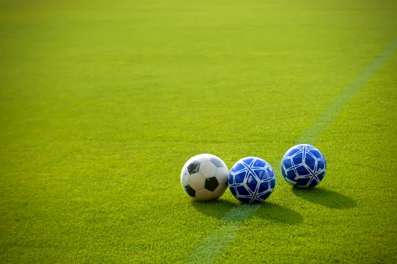 Verschiedene aufgepumpte Sportbälle liegen auf einem Sportplatz, bereit für das nächste Spiel.