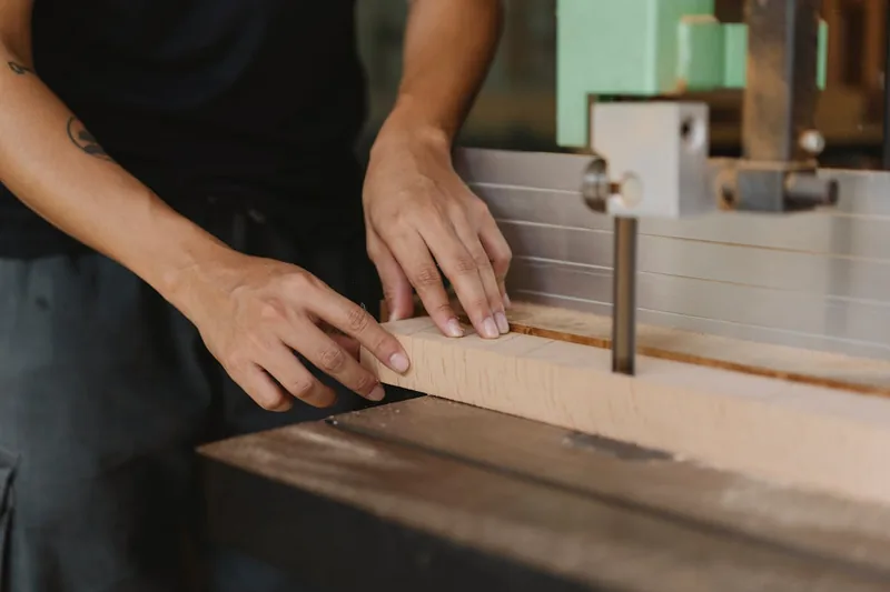 Handwerker sägt präzise ein Holzstück mit einer Bandsäge, Staub und Späne fliegen.