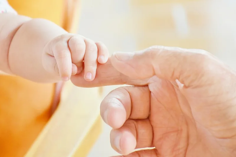 Eine liebevolle Elternhand berührt sanft ein schlafendes Baby in einem Beistellbett und vermittelt Geborgenheit.