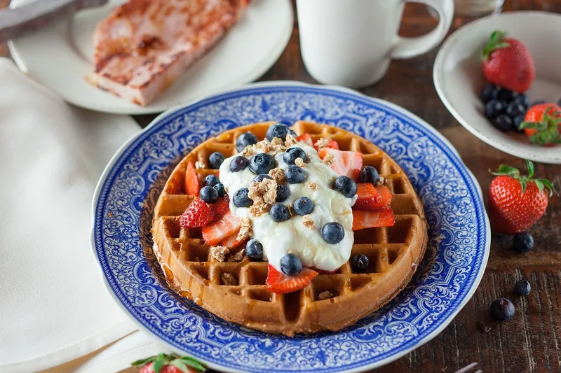 Frisch gebackene belgische Waffeln mit Beeren und Sirup auf einem Teller. Eine gemütliche Frühstücksszene.