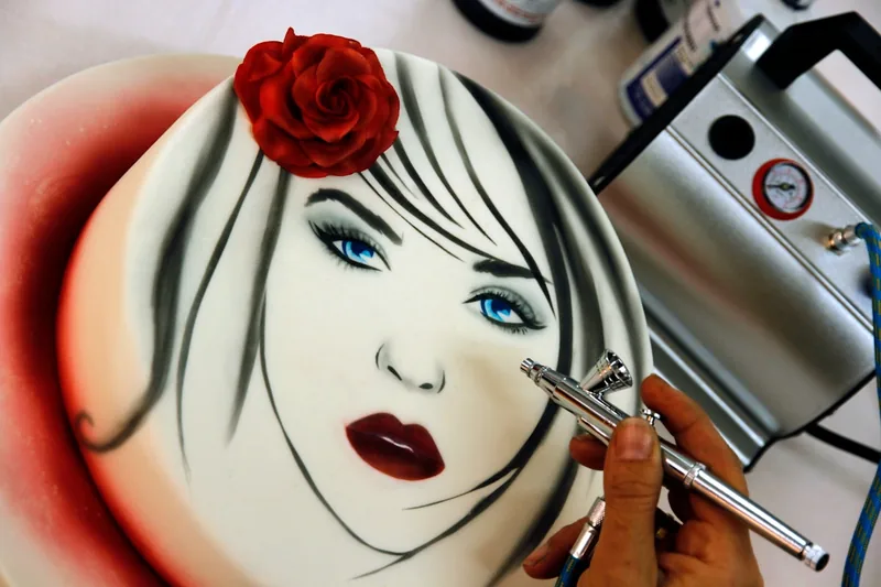 Künstlerhand hält eine Airbrushpistole und sprüht feine Details auf ein Kunstwerk in einem Atelier.