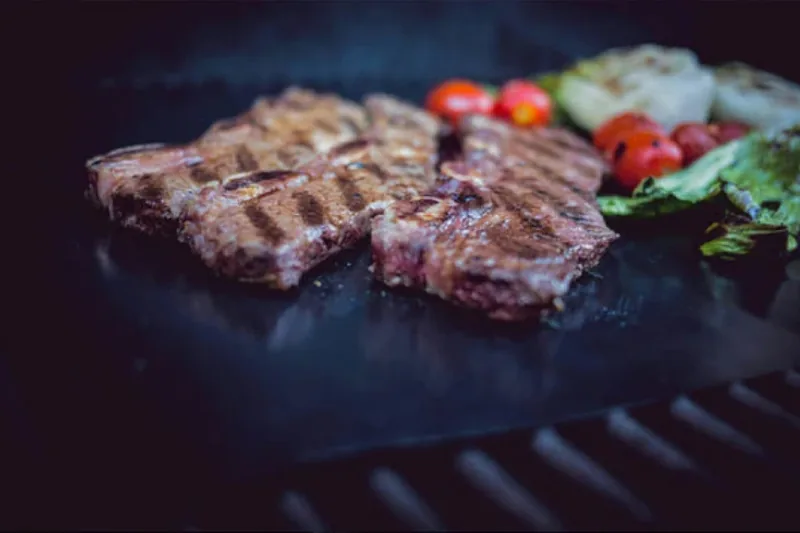 Eine hochwertige BBQ-Grillunterlage liegt auf einem heißen Grillrost, bereit für das Grillgut.