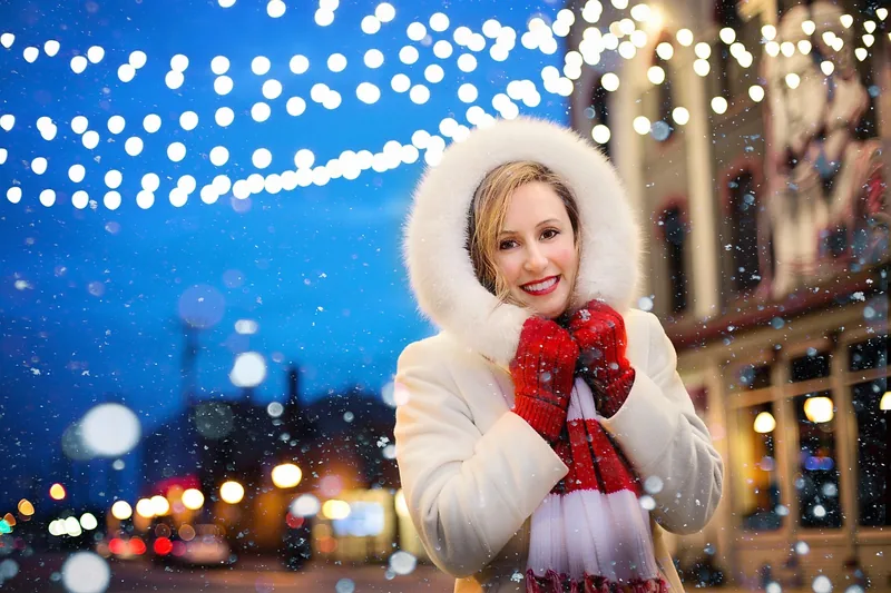 Eine Frau trägt einen leuchtenden Weihnachtspullover für Damen mit kleinen Lichtern und Glocken, im Innenbereich.