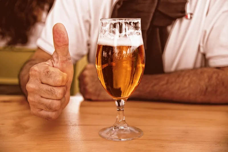 Ein Glas frisch gezapftes, selbstgebrautes Bier steht auf einem Holztisch, im Hintergrund eine gemütliche Wohnzimmer-Atmosphäre.