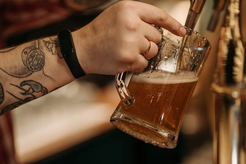 Eine Person zapft frisches, gekühltes Bier aus einem Bierkühler in ein Glas.
