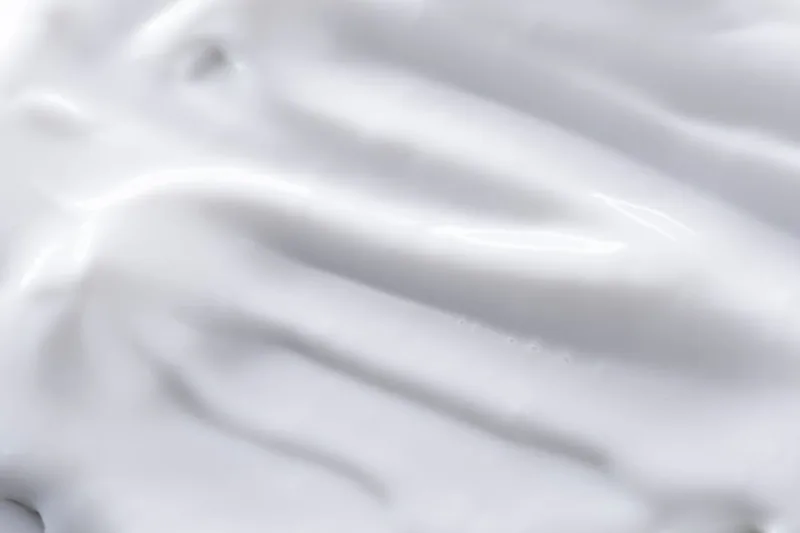 Nahaufnahme der cremigen Textur eines Bio-Shampoos mit angedeuteten natürlichen Inhaltsstoffen für die Haarpflege.