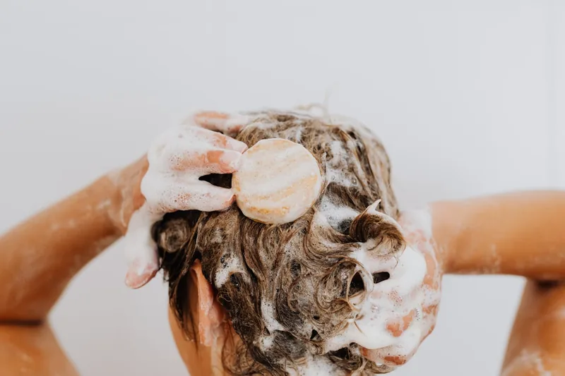 Eine Person wäscht sich sanft die Haare und trägt Bio-Shampoo im Badezimmer auf das nasse Haar auf.