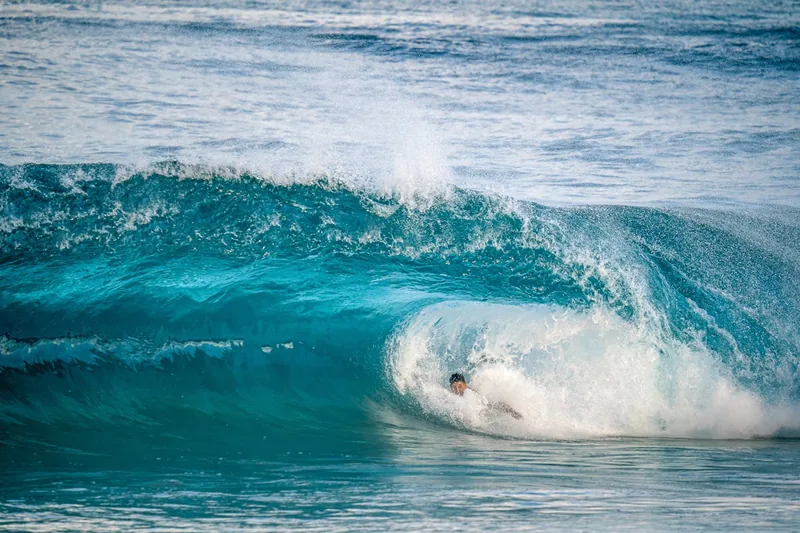 Eine Person reitet auf einem Bodyboard geschickt eine Welle im blauen Ozean bei Sonnenschein.