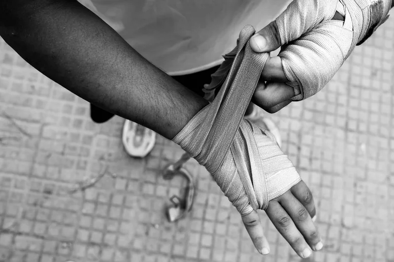 Eine Person wickelt sorgfältig eine Boxbandage um die Hand, zur Vorbereitung auf das Training.