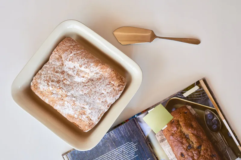 Ein dampfendes, frisch gebackenes Brot in einer Keramikbackform auf einem Küchentisch, umgeben von Backzutaten.
