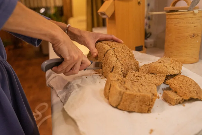 Eine Person schneidet frisches Brot, das gerade aus einem Brottopf auf der Arbeitsplatte kommt.