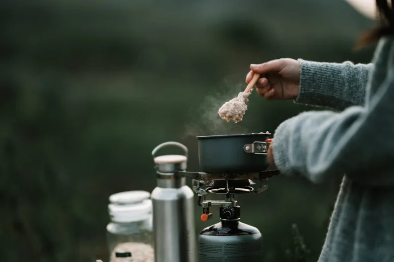 Person bereitet Mahlzeit auf einem Campingkocher zu, demonstriert praktischen Einsatz von Kochgeschirr.