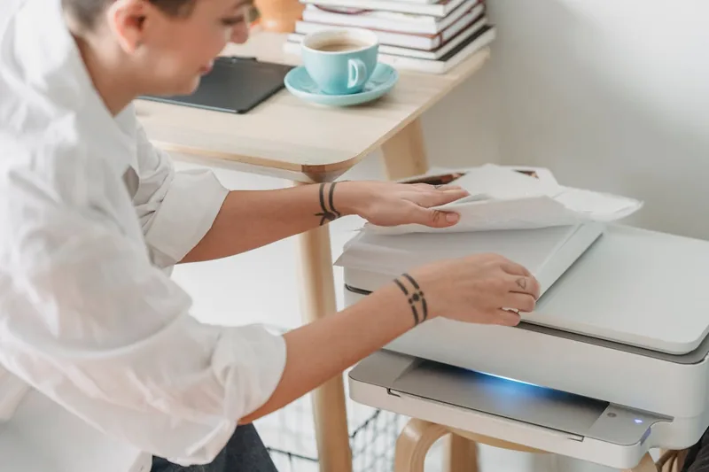 Eine Person legt Papier in einen Drucker, um ein Dokument im Home-Office auszudrucken.