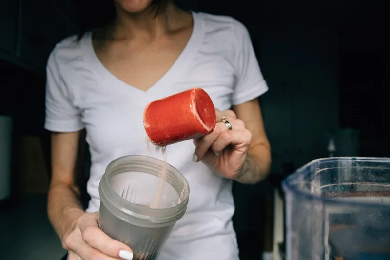 Eine Person mischt Casein-Proteinpulver in einem Shaker mit Flüssigkeit, Hände beim Zubereiten sichtbar.
