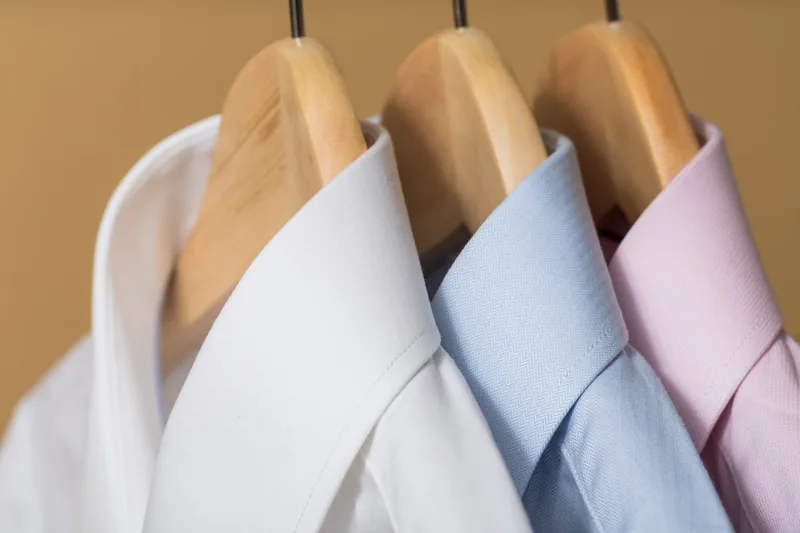 Perfekt gebügelte, faltenfreie Hemden hängen ordentlich im Kleiderschrank, Ergebnis des Bügelns.