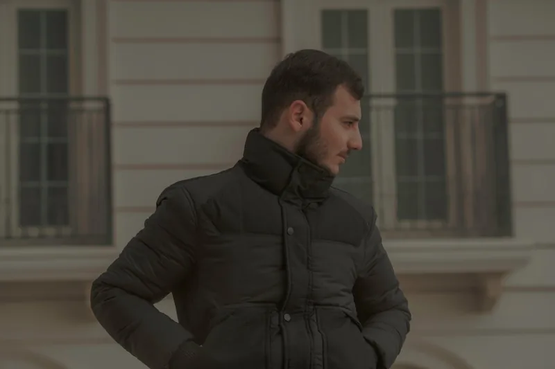 Ein Mann im Profil, der eine Daunenjacke trägt und mit dem Smartphone in einer belebten Winterstadt steht.