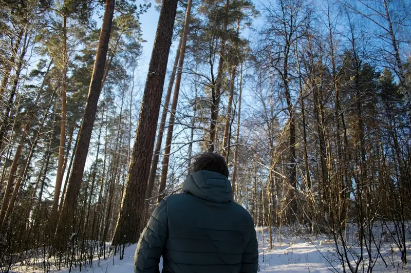 Ein Mann in Daunenjacke wandert durch einen tief verschneiten Winterwald, die Weite der Natur genießend.