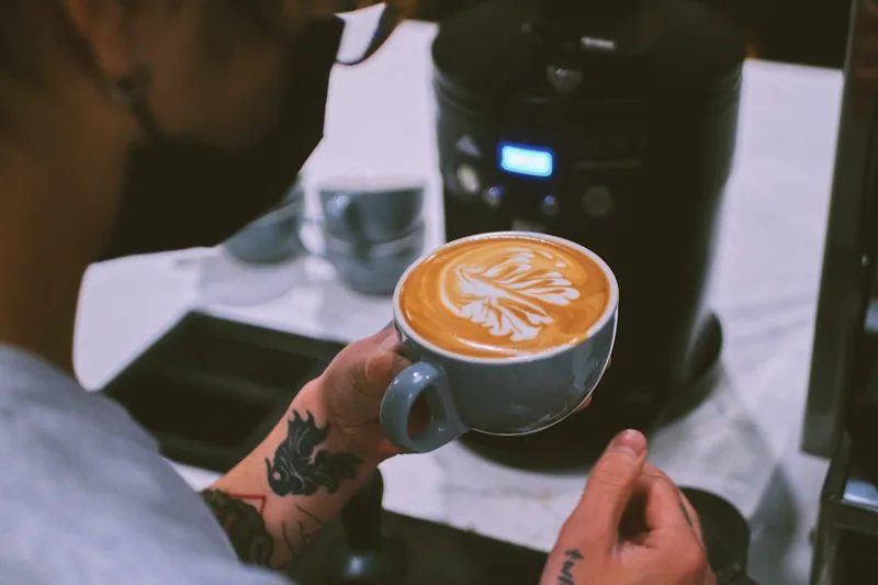 Eine Person bedient einen Kaffeevollautomaten und bereitet einen Latte Macchiato zu.
