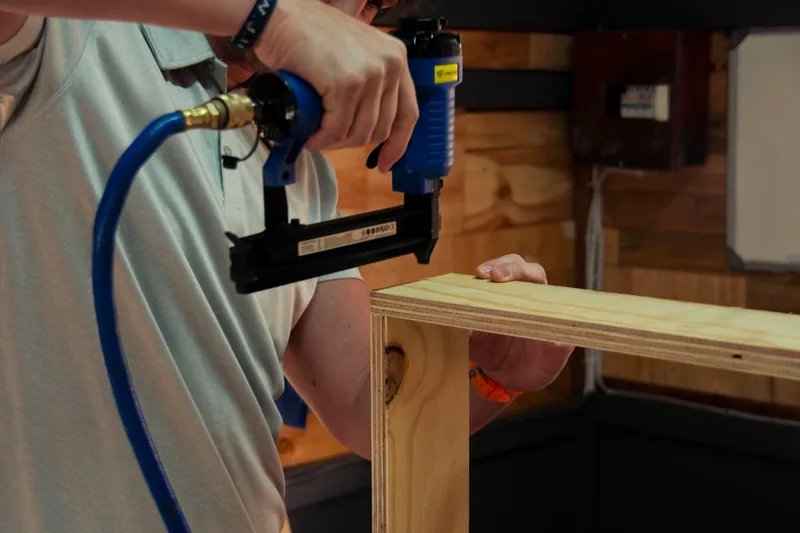 Handwerker beim Befestigen von Holzpaneelen mit einem Druckluftnagler, fokussiert auf die Anwendung.