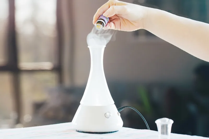 Eine Hand tropft achtsam ätherisches Öl in eine aktive Duftlampe für die Aromatherapie.