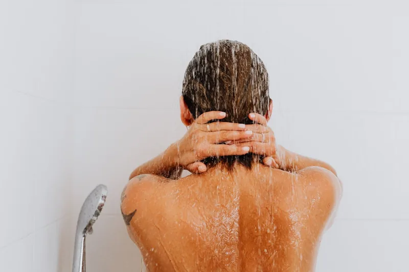 Eine Person unter einem Duschkopf, die den kräftigen Wasserstrahl genießt.
