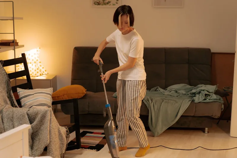 Eine Person saugt mit einem kabellosen Staubsauger staubige Stellen auf einem Holzboden.