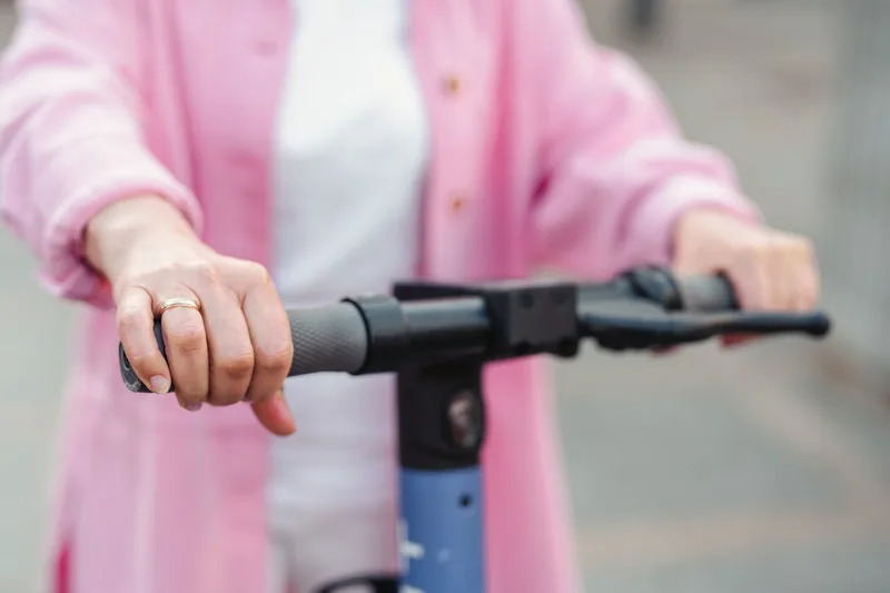 Eine Person fährt einen E-Scooter auf einem Radweg in einer modernen Stadtkulisse.