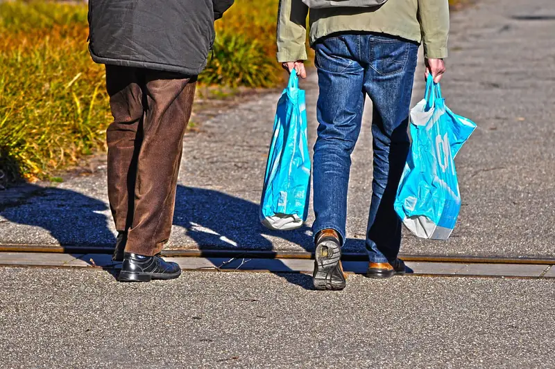 Eine Person trägt einen gefüllten Einkaufskorb durch einen Supermarktgang.
