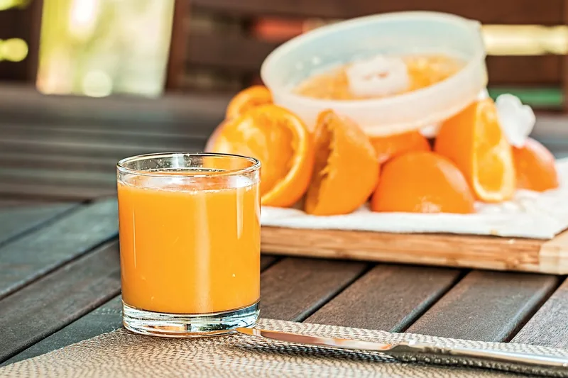 Ein Glas frisch gepresster Orangensaft auf einer Küchentheke, umgeben von Zitrusfrüchten.
