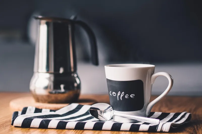 Eine Hand bedient einen elektrischen Espressokocher auf einer modernen Küchenarbeitsplatte, bei der Kaffeezubereitung.