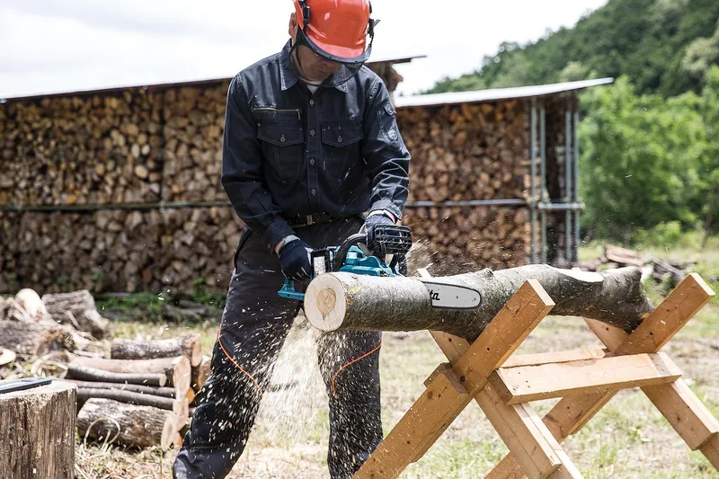 Eine Person sägt Holzstämme mit einer Elektro-Kettensäge im Freien, fokusiert auf die Arbeit.