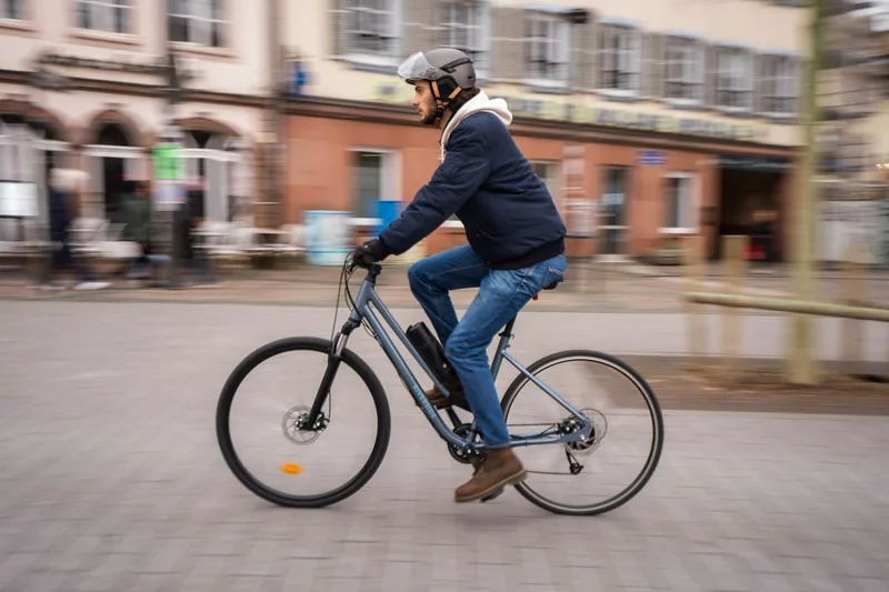 Eine Person fährt entspannt mit einem Elektrofahrrad durch eine belebte Stadtstraße.
