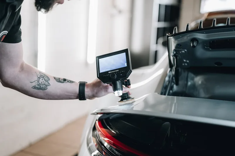 Eine Person inspiziert mit einer Endoskop-Kamera einen Motorraum im Auto.
