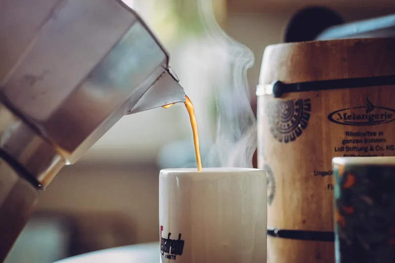 Eine Hand gießt Wasser in einen Espressokocher, bereit für die Kaffeezubereitung.