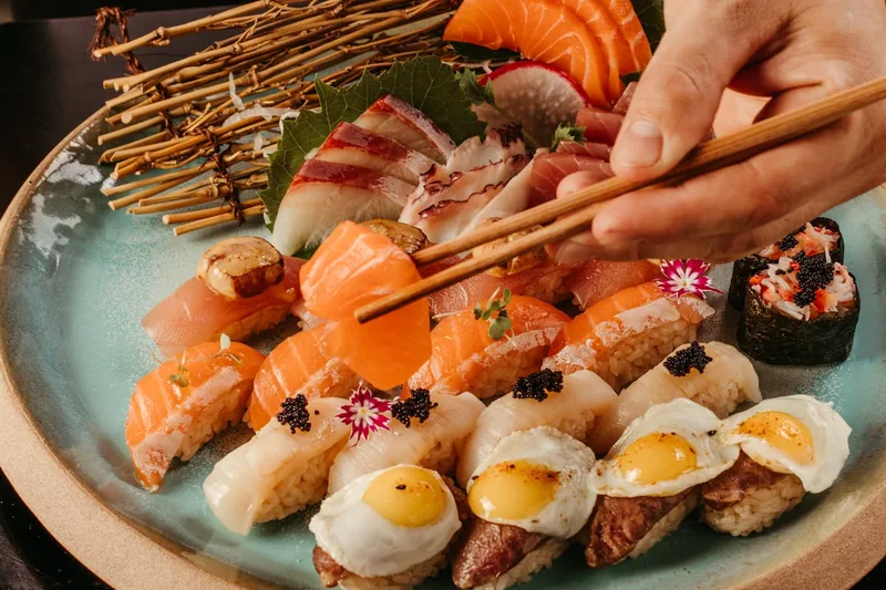 Eine Person hält gekonnt Essstäbchen, um ein Stück frisches Sushi von einem reich gedeckten Teller aufzunehmen.