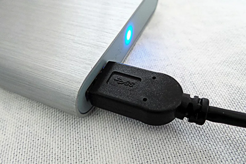Eine Hand schließt eine externe Festplatte an einen Laptop an, symbolisiert Datensicherung.