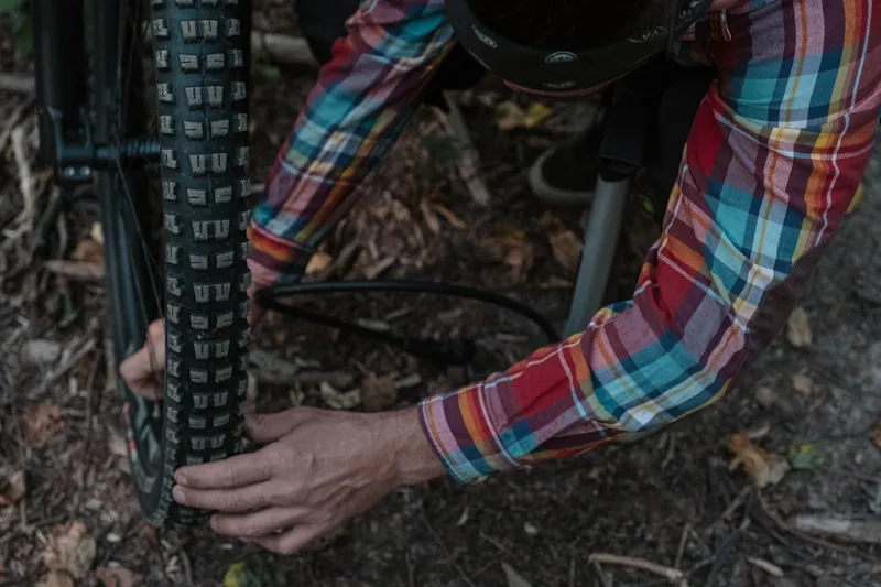 Eine Person repariert mit dem Fahrrad-Reparaturset einen platten Reifen am Hinterrad eines Mountainbikes.